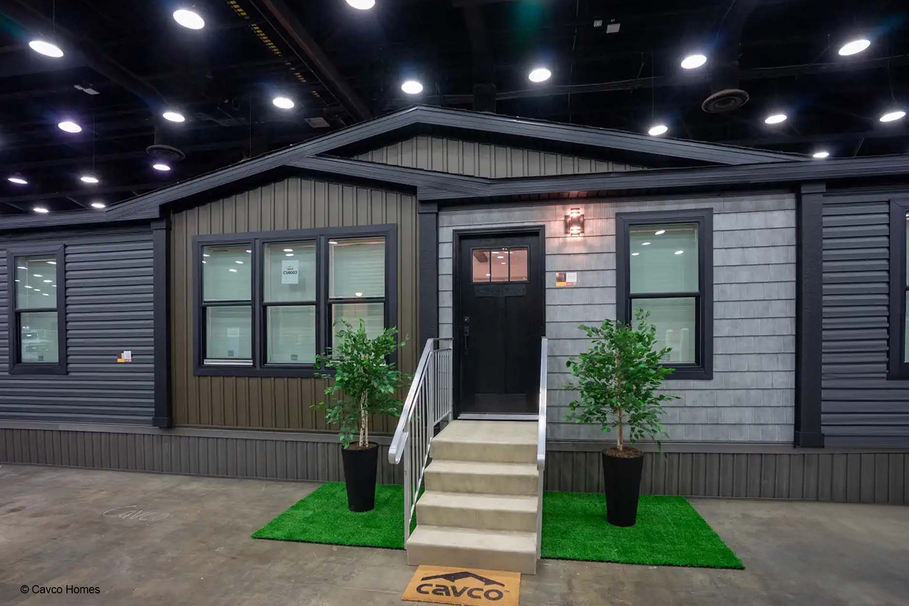 Modern manufactured home with gray siding, a black door, and steps flanked by two potted plants indoors offers stylish comfort and functional design.